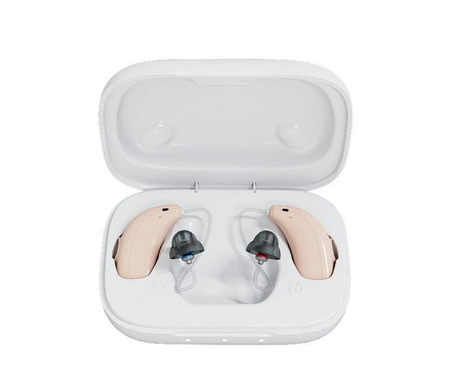A pair of beige behind-the-ear hearing aids with dark gray ear tips, displayed inside an open white charging case on a solid white background.